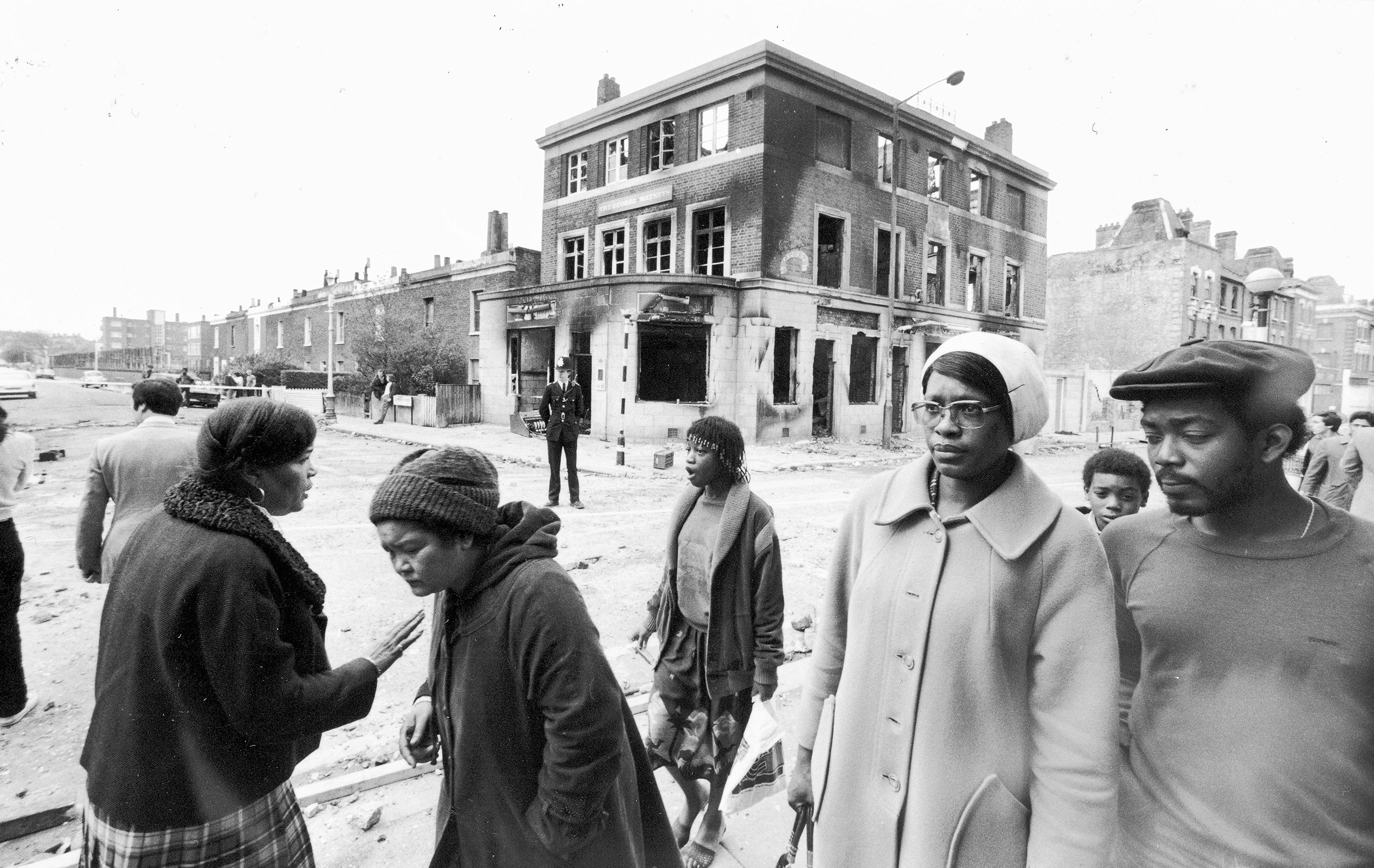 In the aftermath of the 1981 Brixton Riots, residents walk past a burnt-out pub after the second night of unrest, April 13, 1981. Photo via Keystone/Hulton Archive/Getty Images.